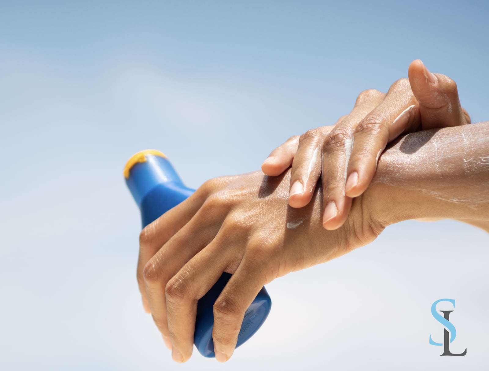 Person applying sunscreen to their arm outdoors under a clear blue sky